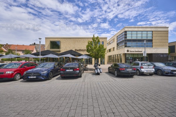 Taunus Sparkasse Anstalt des öffentlichen Rechts, Stadtbücherei, Geschäftsgebäude, moderne Architektur, Kókkos Café und Meze, Außenbereich einer Gastronomie mit Sonnenschirmen, Laterne, Parkplatz mit Autos und Motorrad, Straße aus Betonpflastersteinen, Stadtbäume, blauer Himmel, Altocumuluswolken, Nimbostratuswolken, Kellereiplatz, Hofheim am Taunus, Main-Taunus-Kreis, Hessen, Deutschland