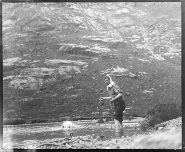 Person crawling across river stream secured by man holding a rope mountain exploration c 1900 possibly Cuillin mountains, Skye, Scotland, UK