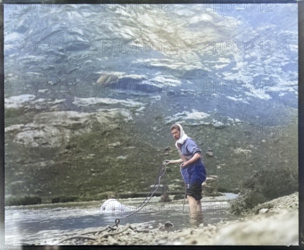 Person crawling across river stream secured by man holding a rope mountain exploration c 1900 possibly Cuillin mountains, Skye, Scotland, UK colourised image