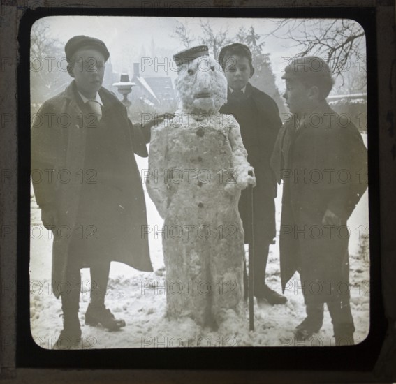 Magic lantern slide three boys making a snowman in a garden, England, UK c 1900-1910