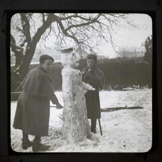 Magic lantern slide two boys making a snowman in a garden, England, UK c 1900-1910