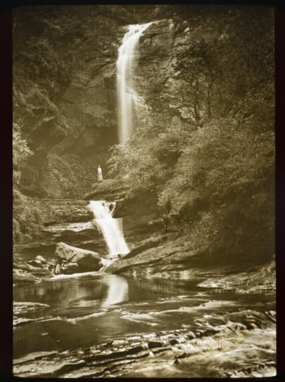 Magic lantern slide c 1900-1910 woman standing in distance beneath waterfall in rocky river gorge Glenashdale lower falls, Isle of Arran, Scotland, United Kingdom