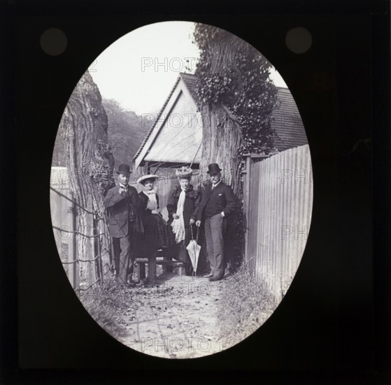Magic lantern slide two well dressed couples one older one younger standing in alleyway in rural location UK circa 1900