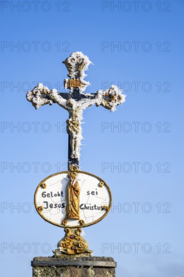 Crucifix with hoarfrost in front of blue sky at sunshine in winter, Bavaria, Germany