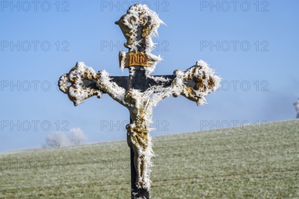 Crucifix with hoarfrost in front of blue sky at sunshine in winter, Bavaria, Germany