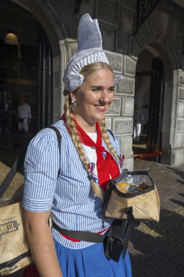 Smiling woman in traditional traditional costume with traditional headgear in front of a historic building, former city scales, cheese market, Alkmaar, Alkmar, Noord-Holland, North Holland, Netherlands
