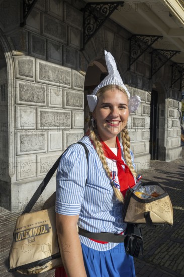 Woman in traditional dress and headdress smiling in front of a historic building, former city weigh house, cheese market, Alkmaar, Alkmar, Noord-Holland, North Holland, Netherlands