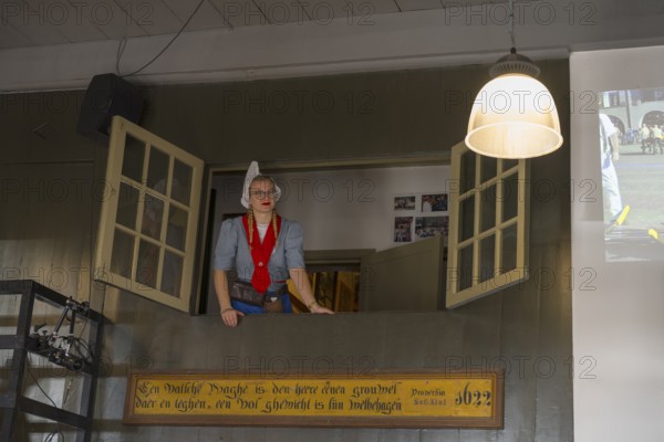 A woman in traditional traditional costume looks out of an open window in a room with traditional decoration, former city weigh house, cheese market, Alkmaar, Alkmar, Noord-Holland, North Holland, Netherlands