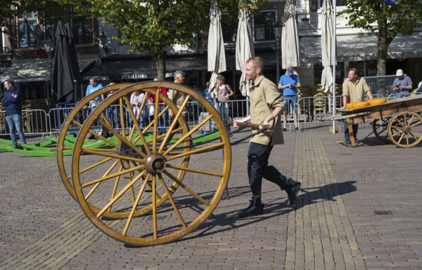 Man pushing large wooden cart wheel at a market in sunny weather, Wooden cart wheel for cheese transport, Cheese, Cheese market, Alkmaar, Alkmar, Noord-Holland, Noord-Holland, Netherlands