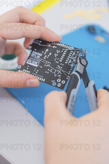 Person holds a circuit board and works on it with pliers on a blue mat