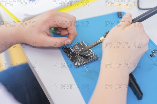 A person solders a circuit board with a soldering iron, surrounded by electronic parts