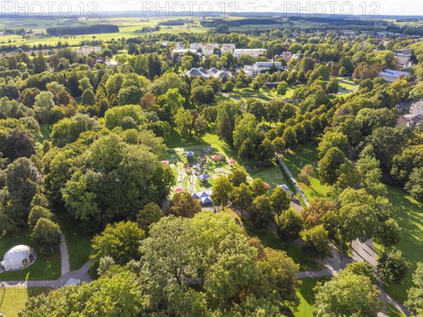 Aerial view of a green park landscape with various trees and buildings in the background under a cloudy sky, Bad Dürrheim, Germany