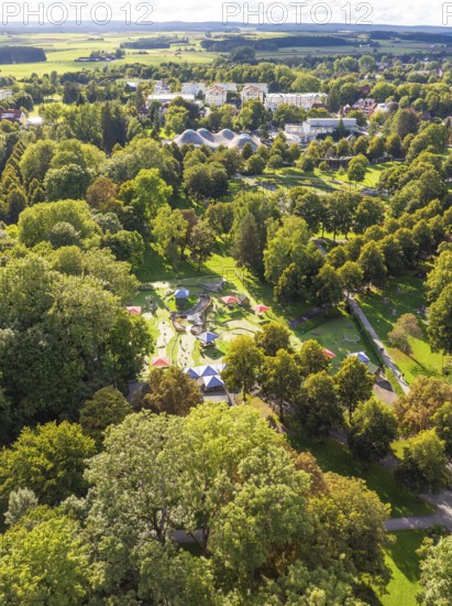 View of a wooded area with embedded park and buildings in the background under a slightly cloudy sky, Bad Dürrheim, Germany