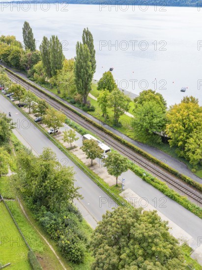 Road and parallel railway line next to a lake, surrounded by trees, Lake Constance Germany