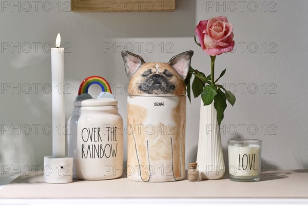 Germany - August 30th 2025: Custom pet dog urn shaped like a French Bulldog surrounded by candle and rose flower. Decorative memorial for dogs