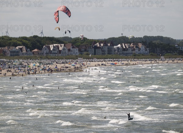 Kitesurfers and holidaymakers on the beach and in the sea, waves, beach chairs, houses in the background, Warnemünde, Rostock, Mecklenburg-Vorpommern, Germany