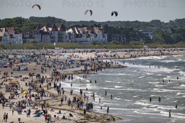 Lively beach with holidaymakers in the sea and on the beach, kite surfers in the surf, Warnemünde, Rostock, Mecklenburg-Vorpommern, Germany