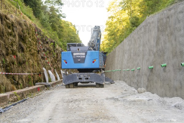 Blue excavator on a construction site between wooded earth slopes, Hermann Hessebahn construction site, Calw, Germany