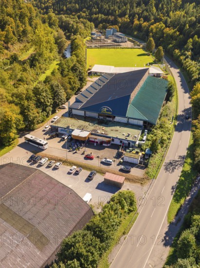 Industrial building with adjacent car park and green landscape, light roof colour, surrounded by a sunny day, Polarion Ice Stadium, Bad Liebenzell, Black Forest, Germany