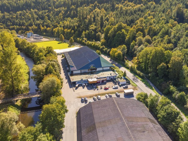 Large building in wooded surroundings near a river, well-frequented car park, bright daylight, Polarion Ice Stadium, Bad Liebenzell, Black Forest, Germany