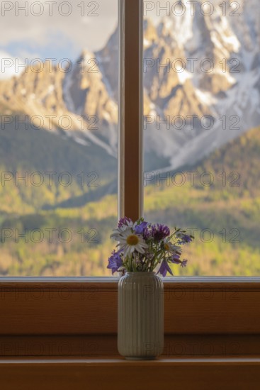 A vase with meadow flowers stands on the windowsill in the background the mountains of the Dolomites, San Candido, Val Pusteria, Sesto Dolomites, Dolomites, South Tyrol, Italy