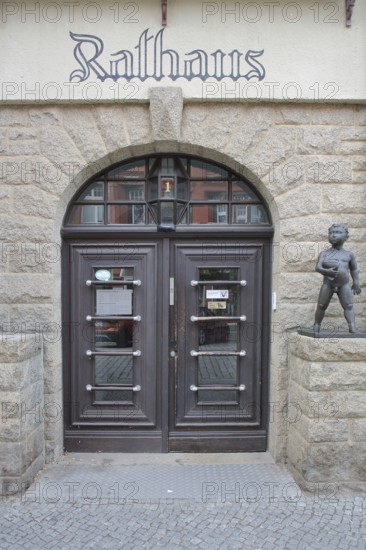 Entrance with cherub to the town hall, front door, inscription, bronze sculpture, nude figure with scroll, Aschersleben, Harz, Saxony-Anhalt, Germany