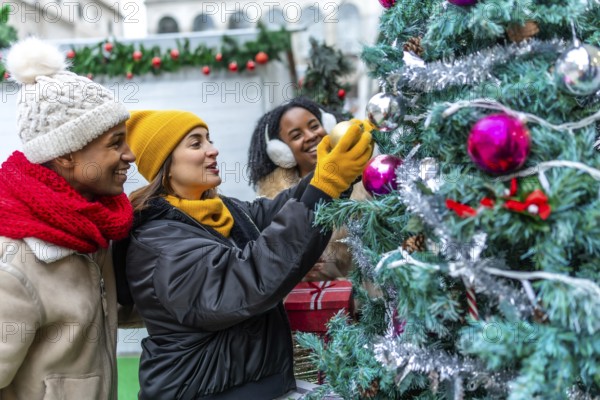 Happy multi ethnic friends gathering at an outdoor christmas market, joyfully decorating a colorful christmas tree together in the winter chill