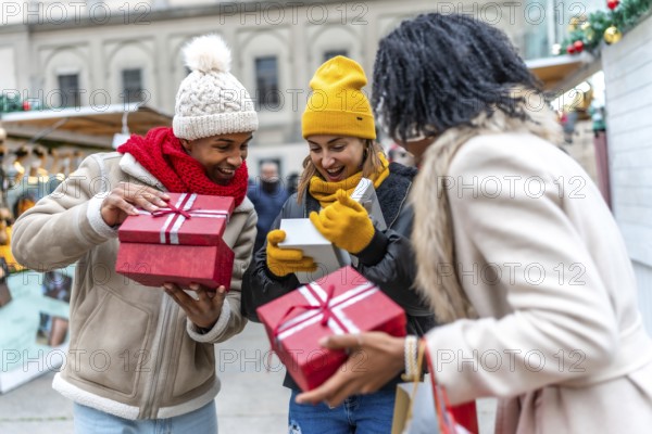 Three happy friends opening christmas gifts at a christmas market, enjoying winter holidays together