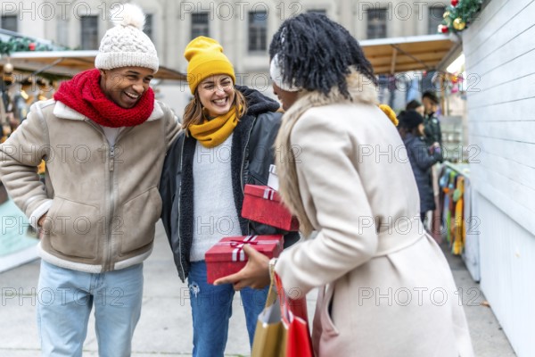 Happy friends exchanging christmas gifts while enjoying a stroll through a festive winter market