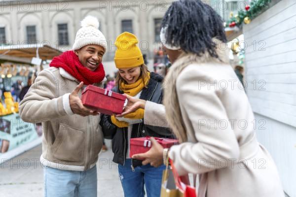 Happy multi ethnic friends exchanging christmas gifts at a christmas market, enjoying winter holidays together
