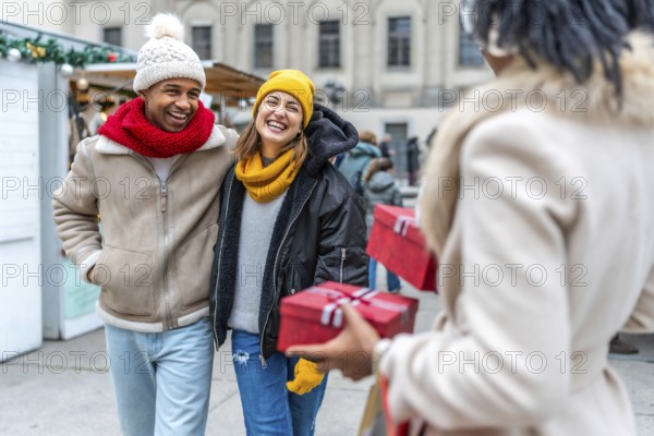 Friends laughing and exchanging christmas gifts at a winter market in the city, enjoying the festive atmosphere