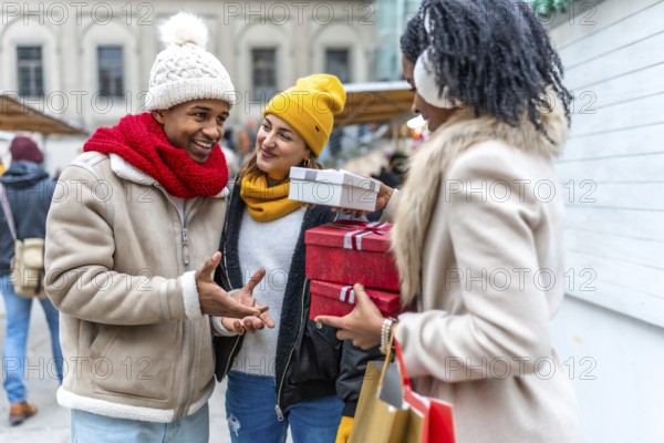 Three friends exchanging christmas gifts and shopping bags at a winter market, enjoying the festive atmosphere