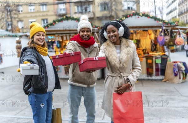 Happy multi ethnic friends showing christmas gifts at a decorated outdoor christmas market