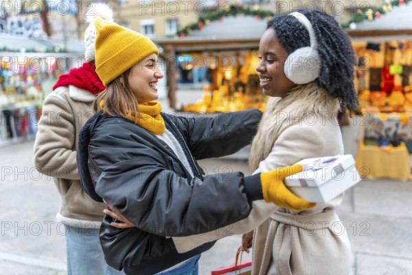 Two happy women exchanging christmas gifts at a christmas market, enjoying winter holidays together