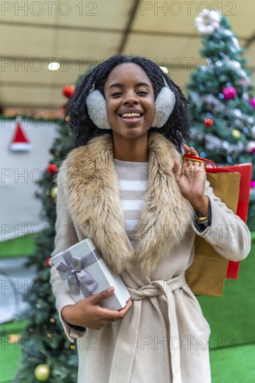 Happy customer holding a christmas present and shopping bags, enjoying winter sales in a decorated city mall