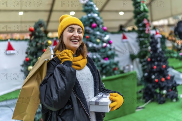 Smiling woman carrying shopping bags and gift box enjoying christmas shopping at a decorated outdoor market