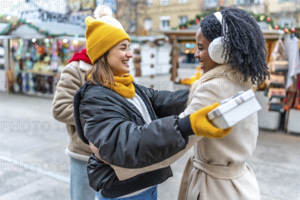 Two happy female friends exchanging christmas presents at a decorated outdoor city market during wintertime