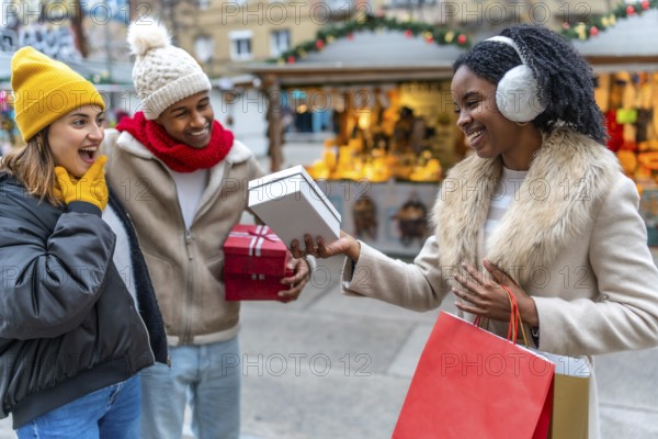 Three happy friends exchanging gifts during christmas shopping in a decorated city center