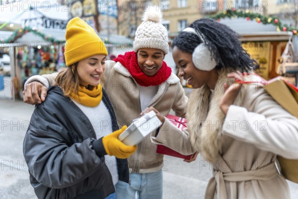 Three joyful friends exchanging gifts at a bustling christmas market, enjoying the festive atmosphere and celebrating the winter holidays together