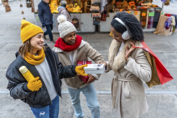 Happy multi ethnic friends joyfully exchanging christmas gifts while shopping together at a bustling winter street market filled with festive cheer
