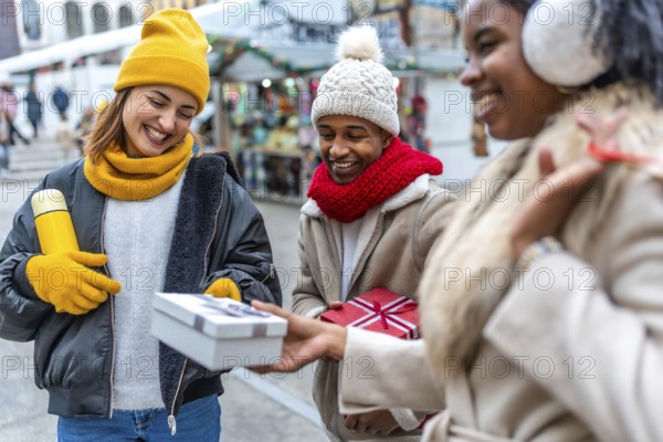 Happy multi ethnic friends exchanging christmas gifts at an outdoor winter market, enjoying the festive atmosphere