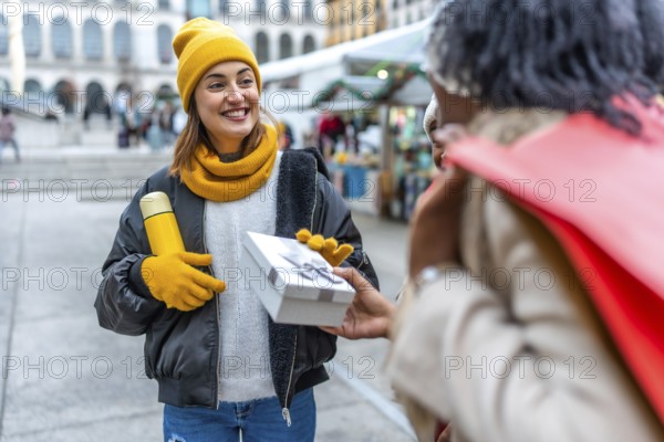 Two friends joyfully exchanging gifts at a bustling christmas market in the city, embracing the festive spirit of wintertime