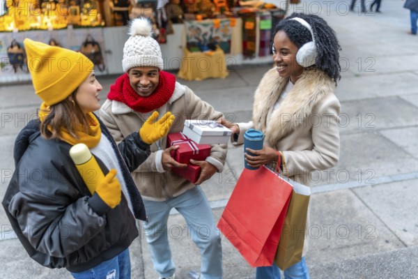 Happy multi ethnic friends exchanging christmas gifts and enjoying hot drinks at a winter christmas market