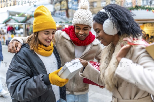 Three happy friends enjoying exchanging christmas gifts at a winter outdoor christmas market