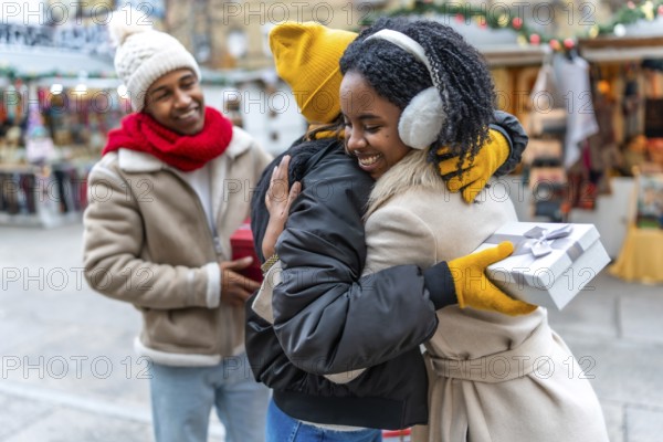 Happy friends exchanging christmas gifts and hugging at a christmas market during winter holidays
