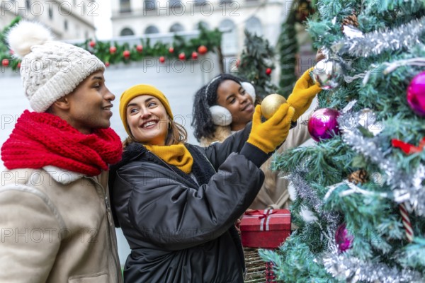 Happy multi ethnic friends decorating christmas tree at outdoor christmas market, wearing winter clothes