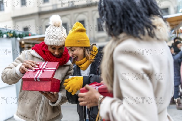 Happy friends joyfully exchanging christmas gifts at a bustling market, celebrating the festive winter season with laughter and warmth