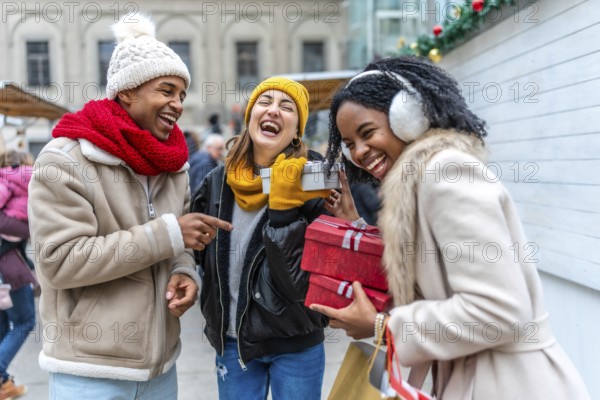 Three friends are having fun exchanging christmas gifts at a winter market, laughing and enjoying the festive atmosphere