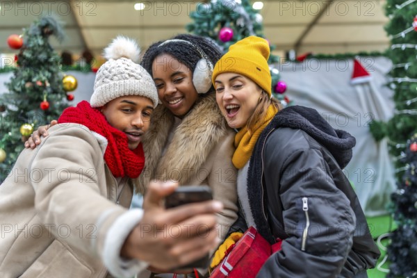 Three cheerful young friends taking a selfie with smartphone in a christmas decorated shopping mall