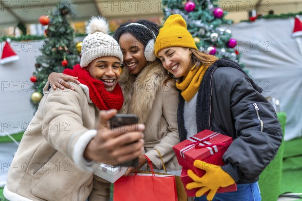 Group of cheerful multi ethnic friends taking a selfie with a smartphone after winter shopping at a christmas market